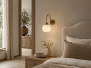 Aveline gooseneck brass wall light beside a warm neutral bed